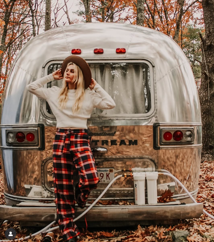 Person standing in front of a vintage Airstream trailer in a forest setting
